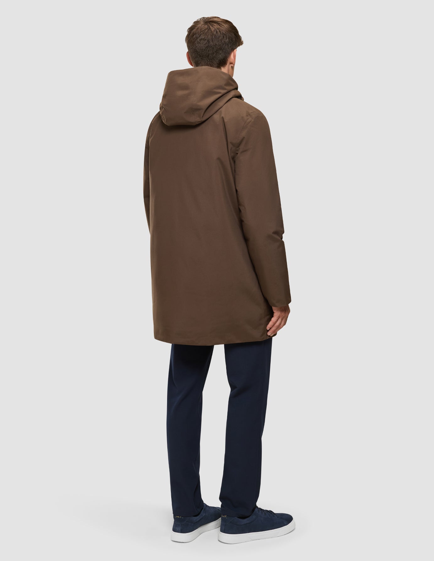 En person set bagfra, iført en Utility Jacket i farven Saddle Brown, marineblå bukser og mørke sneakers.